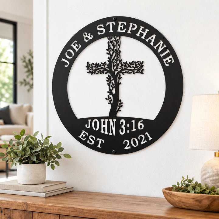 a black metal wall decoration with a tree-like design and the names "Joe & Stephanie" around the edge. The decoration is mounted on a white wall, and there are some decorative items on a wooden table below it.