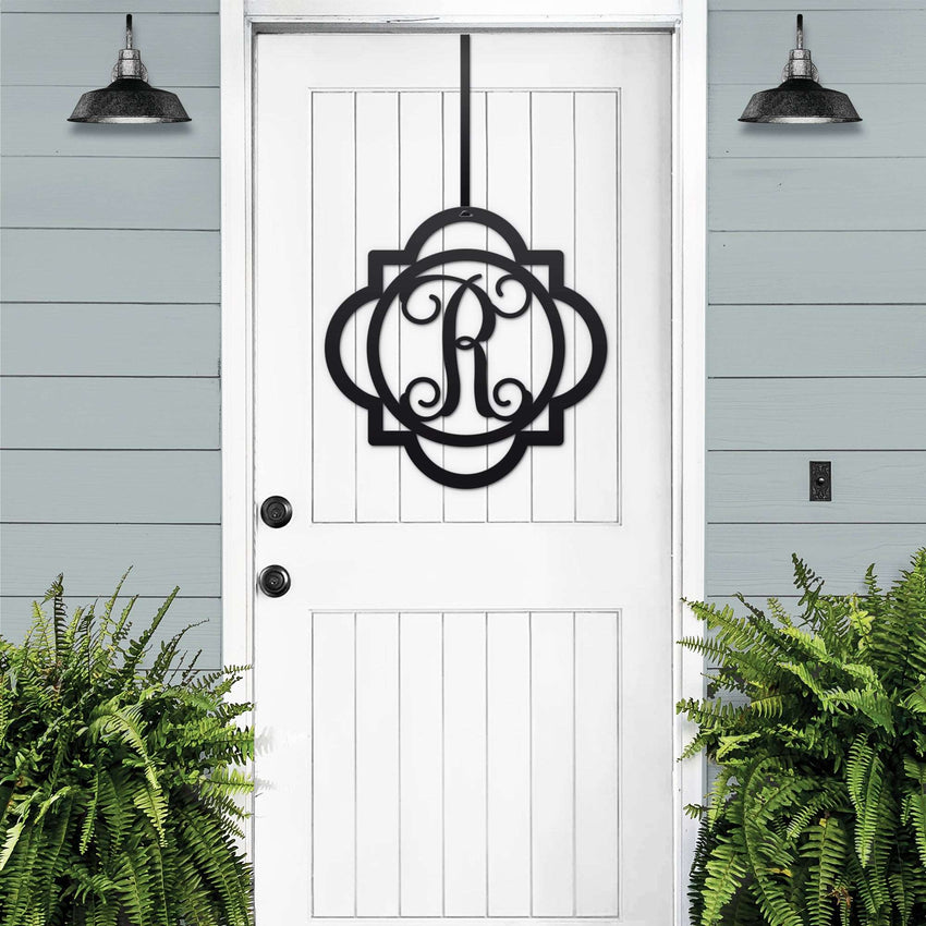 Black monogram door hanger sign with decorative letter R displayed on white farmhouse front door with porch plants