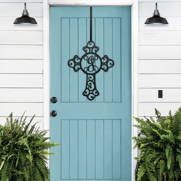 Black cross monogram metal door wreath displayed on a wood door