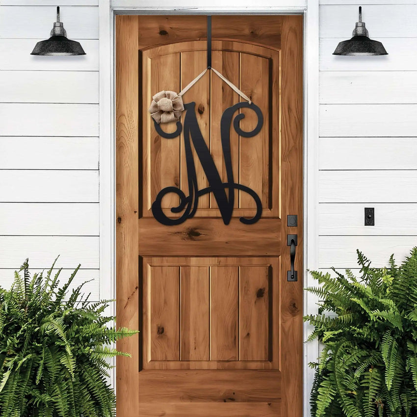 Black personalized metal initial door wreath displayed on a wood front door
