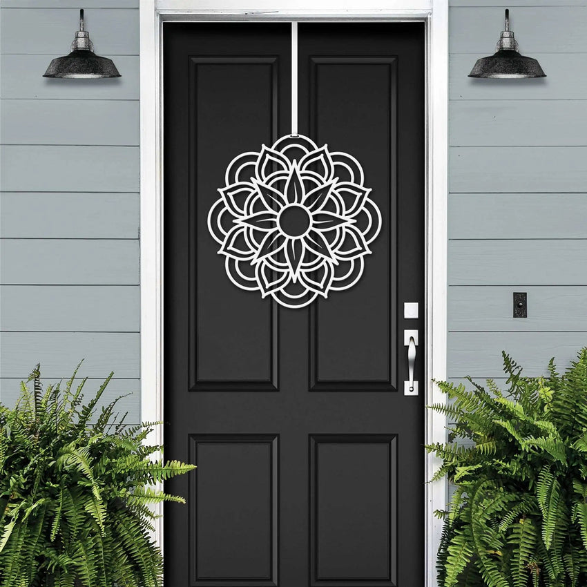 Handcrafted metal flower wreath on black front door, white decorative pattern, gray exterior wall, modern outdoor metal door decor, elegant home entry art