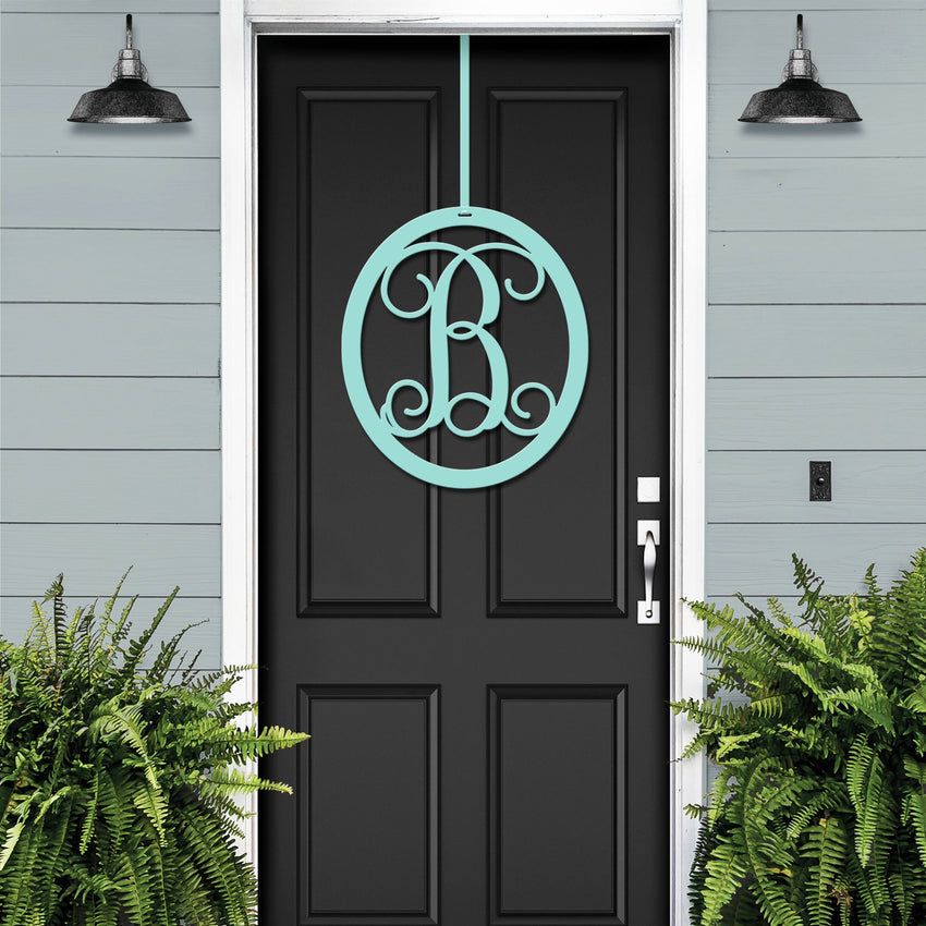 Black oval metal monogram door wreath shown on a green door