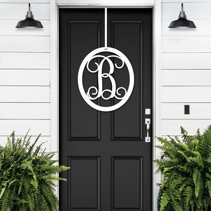 White oval metal monogram door wreath shown on a black door