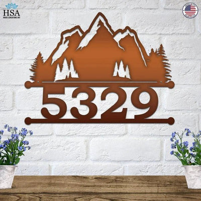 Personalized metal house number sign with mountain design mounted on a white brick wall for outdoor curb appeal, HouseSensationsArt