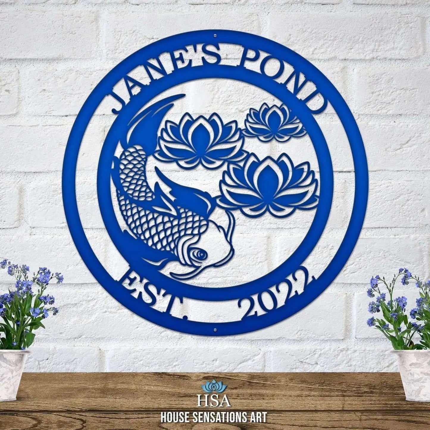 Koi Pond and Lotus Flower Metal Sign - Custom Metal House Number Plaque, showcasing a blue fish and floral design on a white brick wall. Ideal for outdoor decor in gardens, yards, or farms.