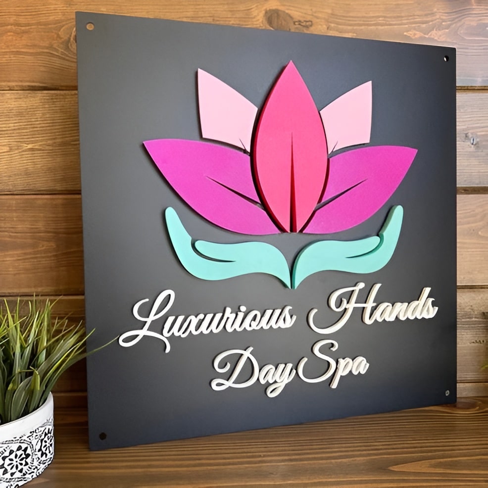 Custom 3D multi-material steel metal sign with pink and green lotus flower design and "Luxurious Hands Day Spa" text mounted on a wooden background – House Sensations Art.