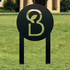 a black sign with a large "B" symbol on it, standing on a grassy lawn.