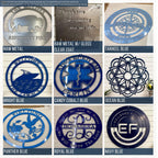 9-panel color sample chart displaying different finishes and shades for custom metal signs. Top row shows Raw Metal with a buffalo design, Raw Metal with Gloss Clear Coat featuring a quote, and Tarheel Blue compass-themed sign. Middle row includes Bright Blue boat sign, Candy Cobalt Blue emergency medical emblem, and Ocean Blue floral mandala design. Bottom row features Panther Blue hummingbird sign, Royal Blue monogram sign, and Navy Blue circular ‘EF’ logo sign