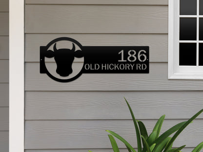 Cattle Farm Monogram Address Sign featuring a black cow head design, affixed on a white wall, showcasing customizable street numbers. Ideal for enhancing farmhouse charm and curb appeal.