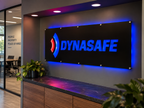 a modern office space with a large illuminated sign for the company "DYNASafe" on the wall. The sign is surrounded by a wooden desk and a potted plant, creating a professional and welcoming atmosphere.