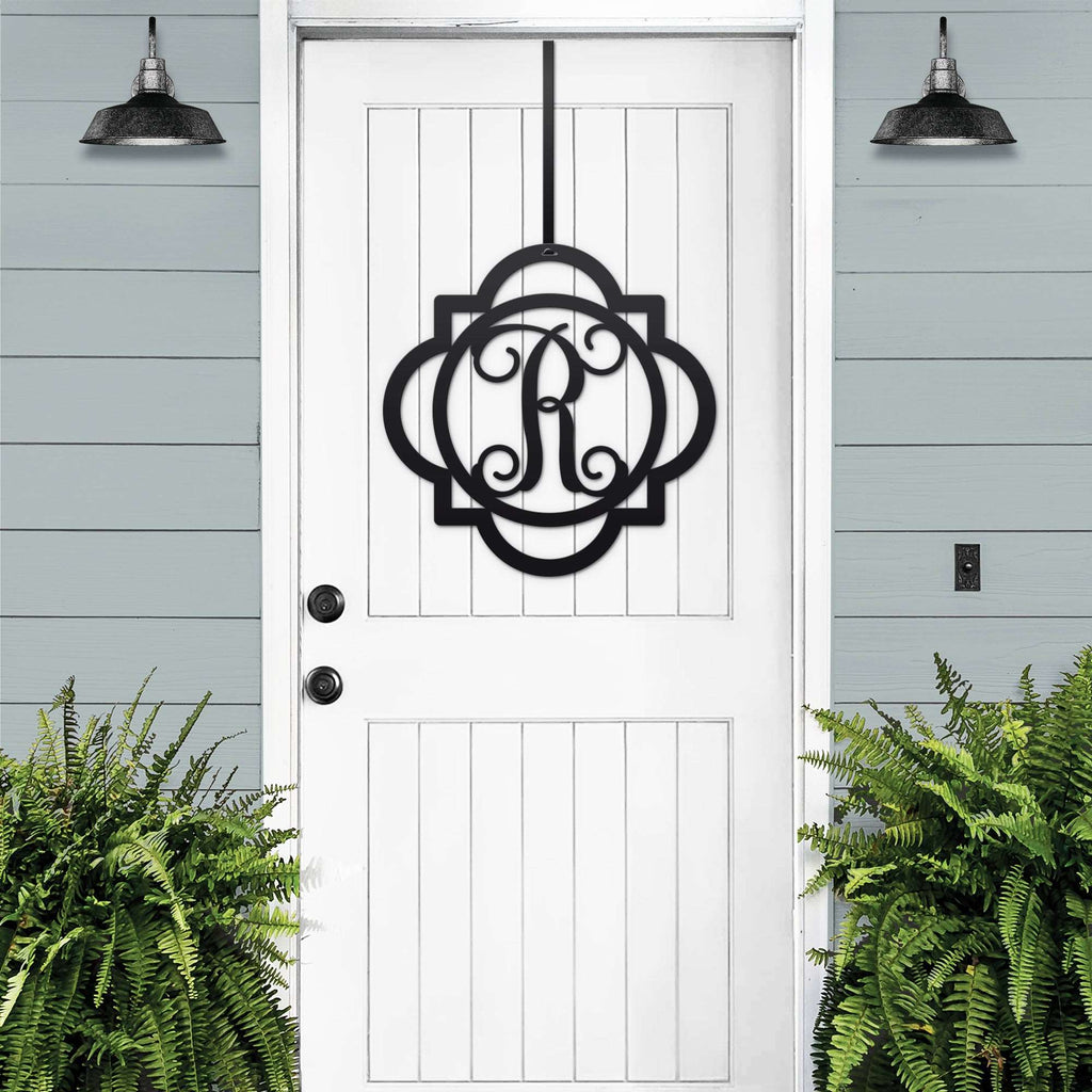 Black monogram door hanger sign with decorative letter R displayed on white farmhouse front door with porch plants