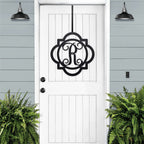 Black monogram door hanger sign with decorative letter R displayed on white farmhouse front door with porch plants