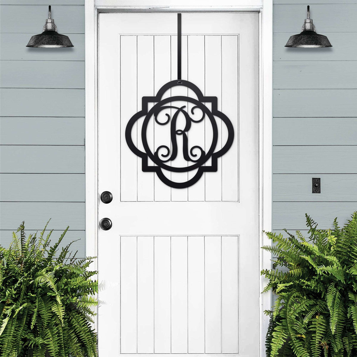 Black monogram door hanger sign with decorative letter R displayed on white farmhouse front door with porch plants