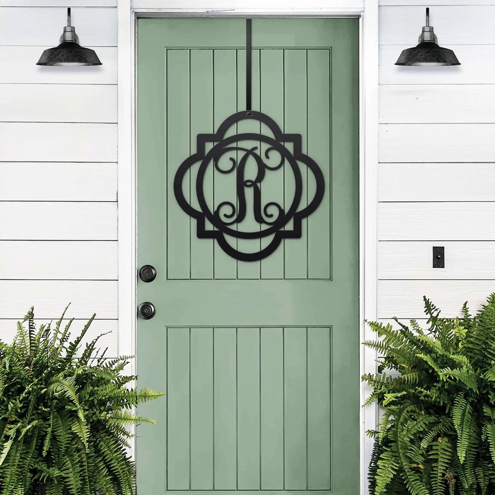 Black monogram metal door hanger with decorative letter R displayed on sage green front door with porch plants