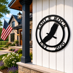 Black personalized Eagle Rock metal sign with Est 2020 displayed on a white porch wall with garden and flag decor