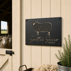Black spotted sheep farm custom metal wall sign mounted on cream barn wall beside sheep barn entrance