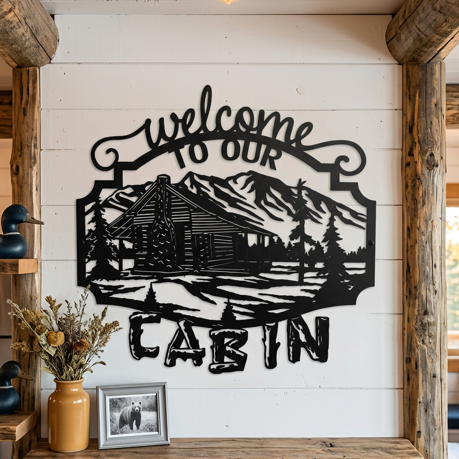 Black cabin mountain metal welcome sign displayed on a white shiplap wall with warm rustic lodge accents