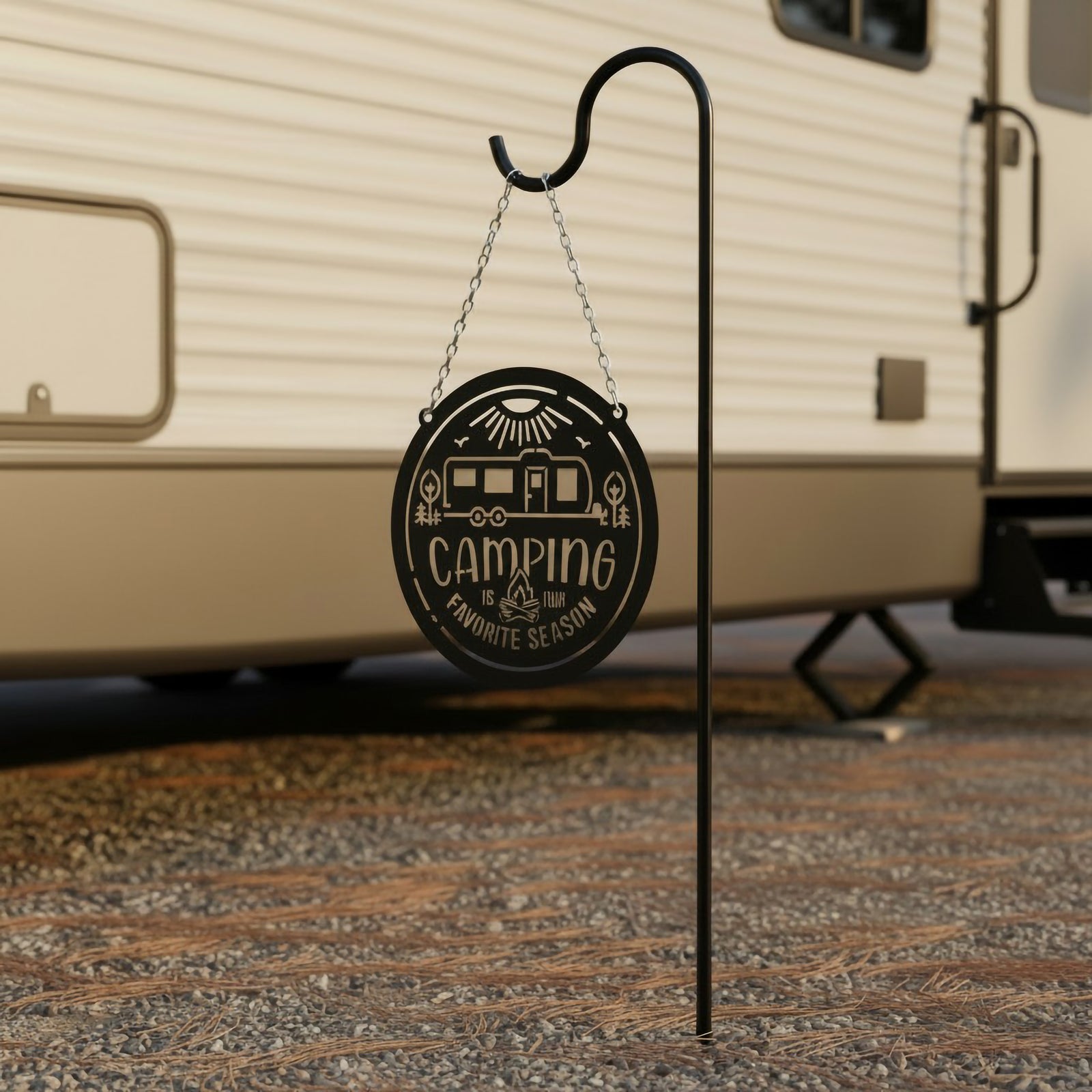 Gloss black camping metal sign suspended from a shepherd hook near an RV trailer featuring a camper, campfire, and Camping Is Our Favorite Season cutout design.