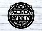 Circular metal sign featuring a camping-themed design with text, displayed on a white wooden background, highlighting rustic style and durable decorative craftsmanship.