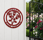 Glossy candy apple red finish of the custom circular rose metal art sign styled on a white vertical wood panel wall next to an ornate black iron garden gate.
