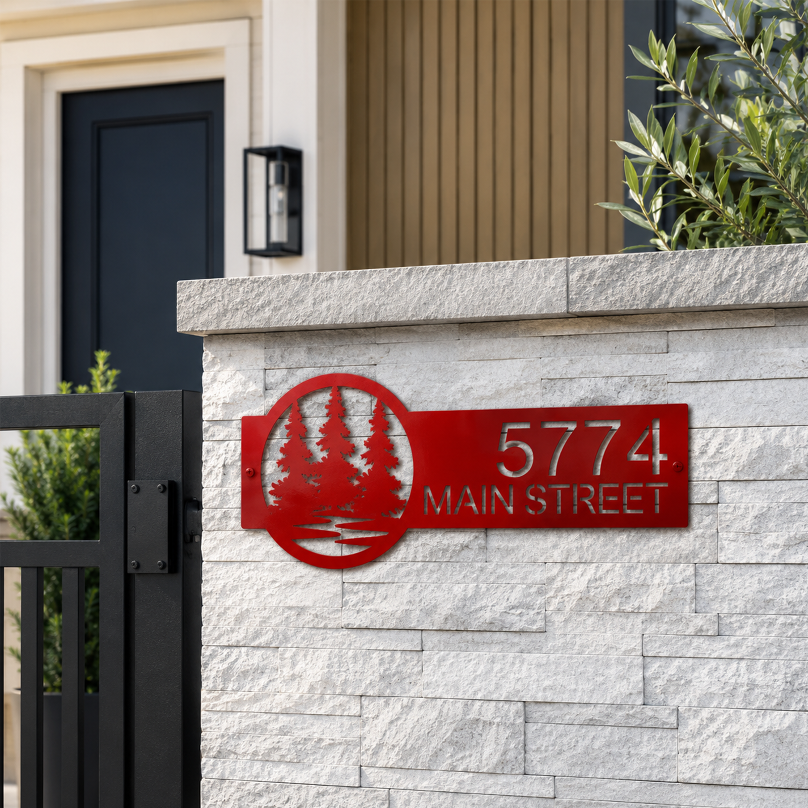 Candy apple red custom metal address sign with pine tree forest design mounted on white stone wall displaying 5774 Main Street