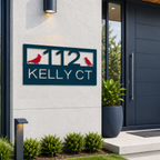 A rectangular metal address plaque in a deep ocean blue finish is mounted on a textured cream exterior wall. The sign displays the cutout text "112 KELLY CT" accented by two bright red cardinal bird silhouettes. A large navy planter sits by a matching modern front door in the background.