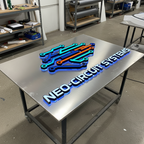 “Neo-Circuit Systems” 3D neon sign on a metal table in a workshop, showcasing custom illuminated signage and channel letter production.