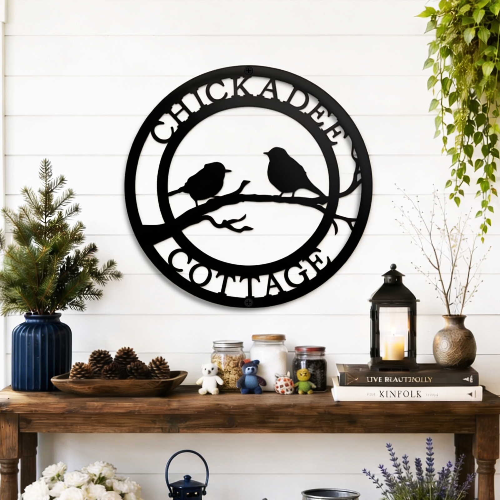Black chickadee cottage metal wall decor with bird silhouette design displayed above rustic farmhouse entryway table with lanterns and plants