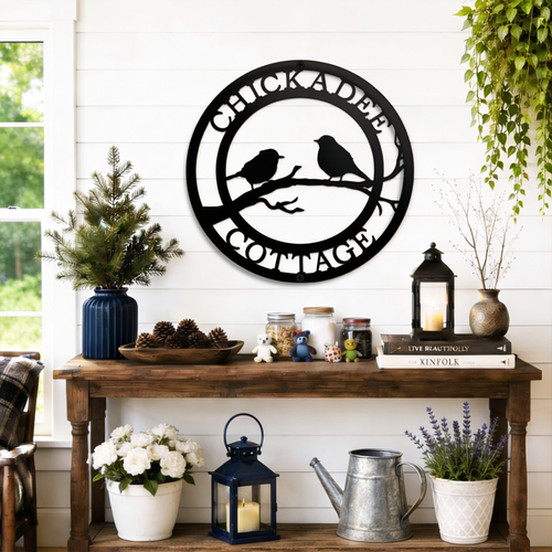 Black chickadee cottage metal wall decor with bird silhouette design displayed above rustic farmhouse entryway table with lanterns and plants