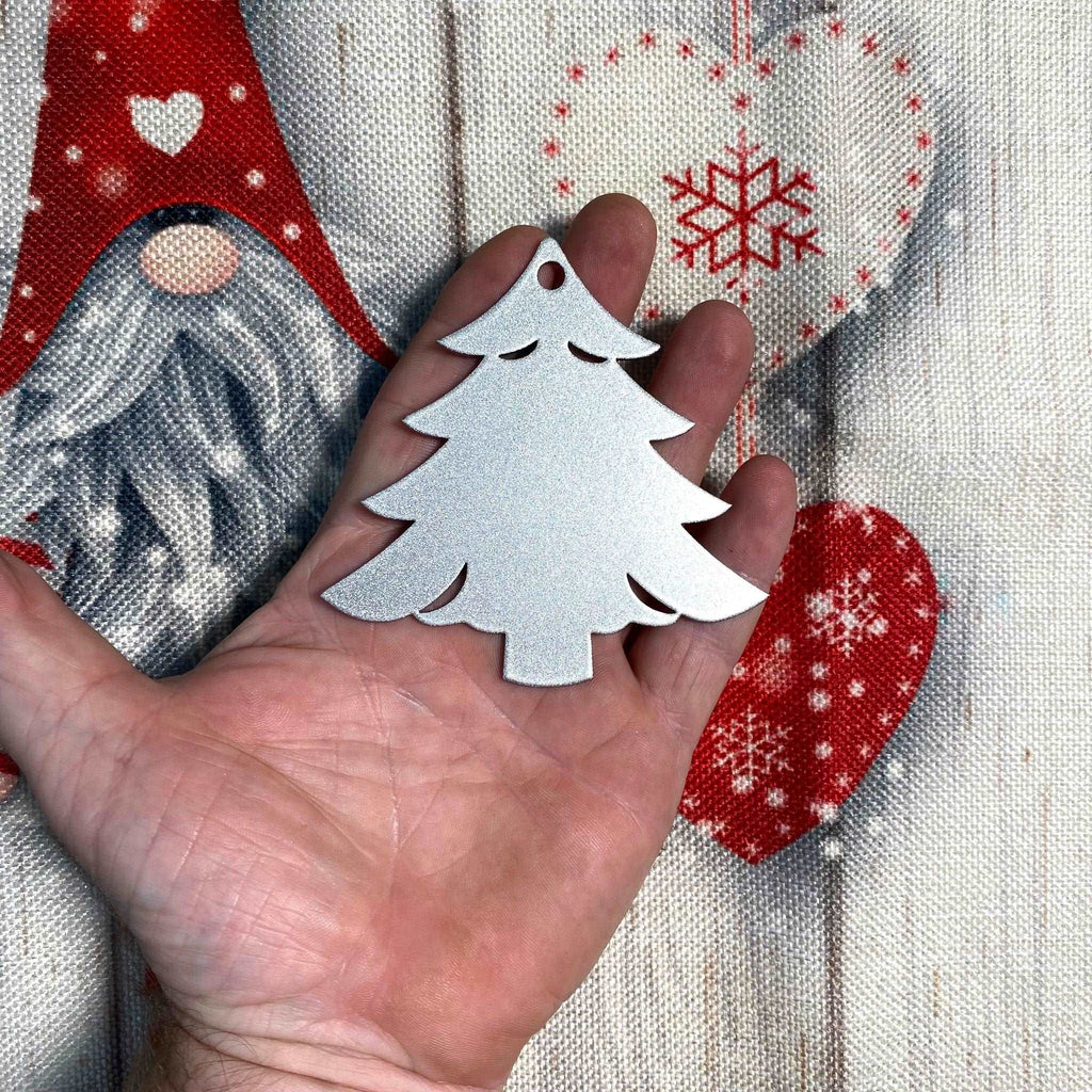 Hand holding a silver Christmas tree ornament against a festive holiday background with soft lights and greenery, creating a warm seasonal atmosphere.