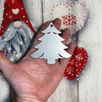 Hand holding a silver Christmas tree ornament against a festive holiday background with soft lights and greenery, creating a warm seasonal atmosphere.