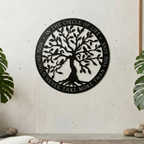 circular matte black metal sign featuring an intricate Tree of Life silhouette is mounted on a light beige exterior wall column. The outer border contains the cut-out quote, "IN THE CIRCLE OF LIFE, YOU SHOULD NEVER TAKE MORE THAN YOU GIVE." Lush green bamboo plants stand in the background on either side of a wooden door.