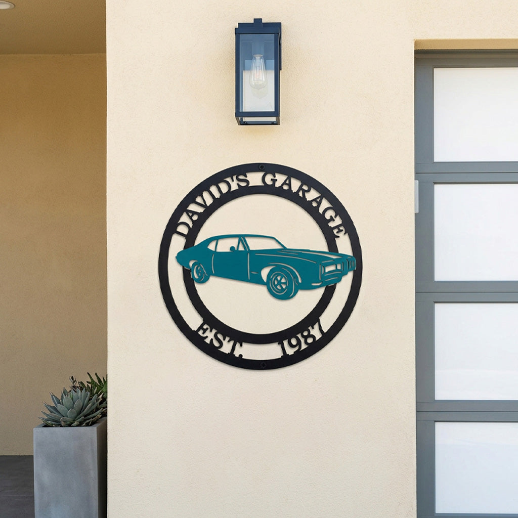 Custom metal garage wall sign featuring classic muscle car silhouette with personalized garage name and established date displayed on outdoor house wall near garage entrance