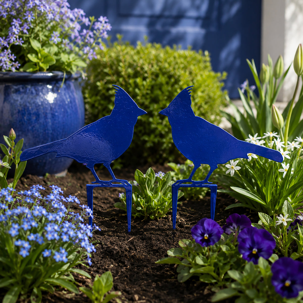 Cobalt blue cardinal metal garden stakes displayed among colorful flowers and outdoor plants