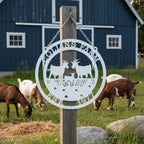 White Collins Farm goat ranch metal sign hanging on wood post with barn and goats in pasture