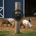 Black Collins Farm round goat metal sign hanging on wood post with goats and barn in farm setting