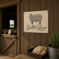 Cream spotted sheep farm metal wall art mounted on dark wood barn wall with sheep barn and wool basket nearby
