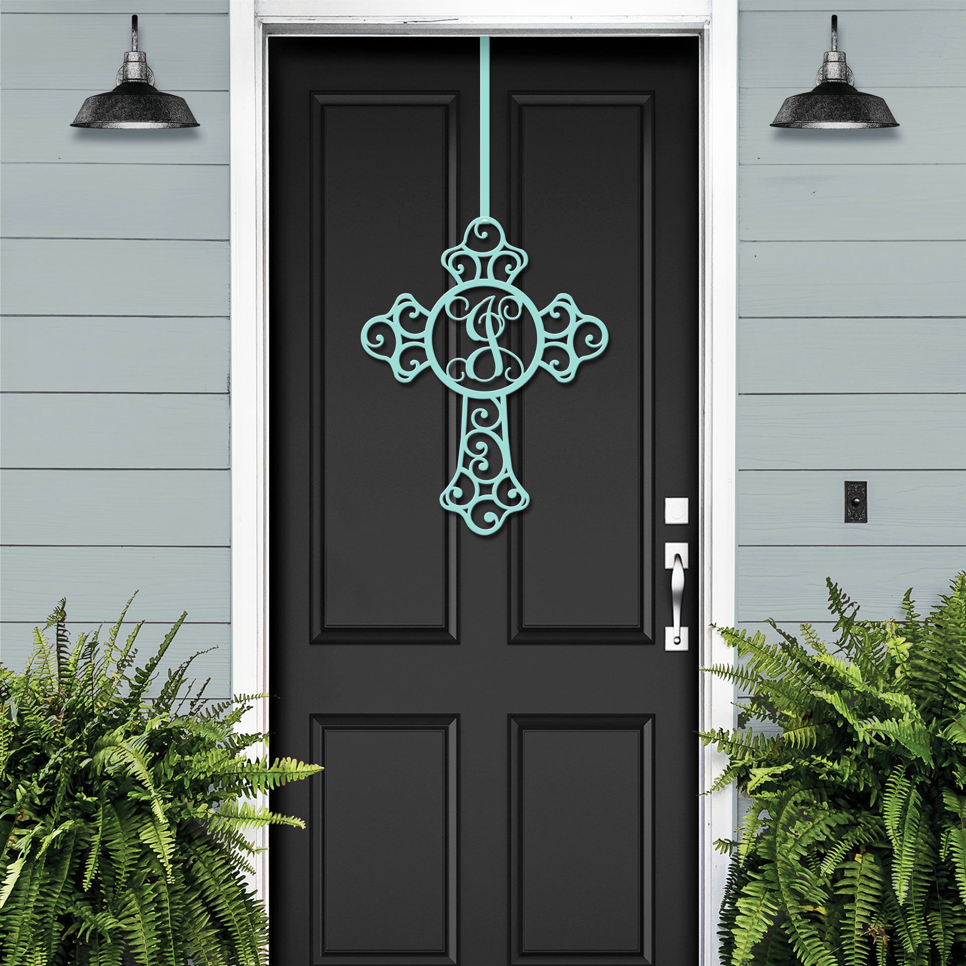 Custom Swirl Monogram Cross Door Sign - Personalized Metal Sign prominently displayed on a white door, accompanied by a lush green plant, capturing its elegant craftsmanship for home and garden decor.