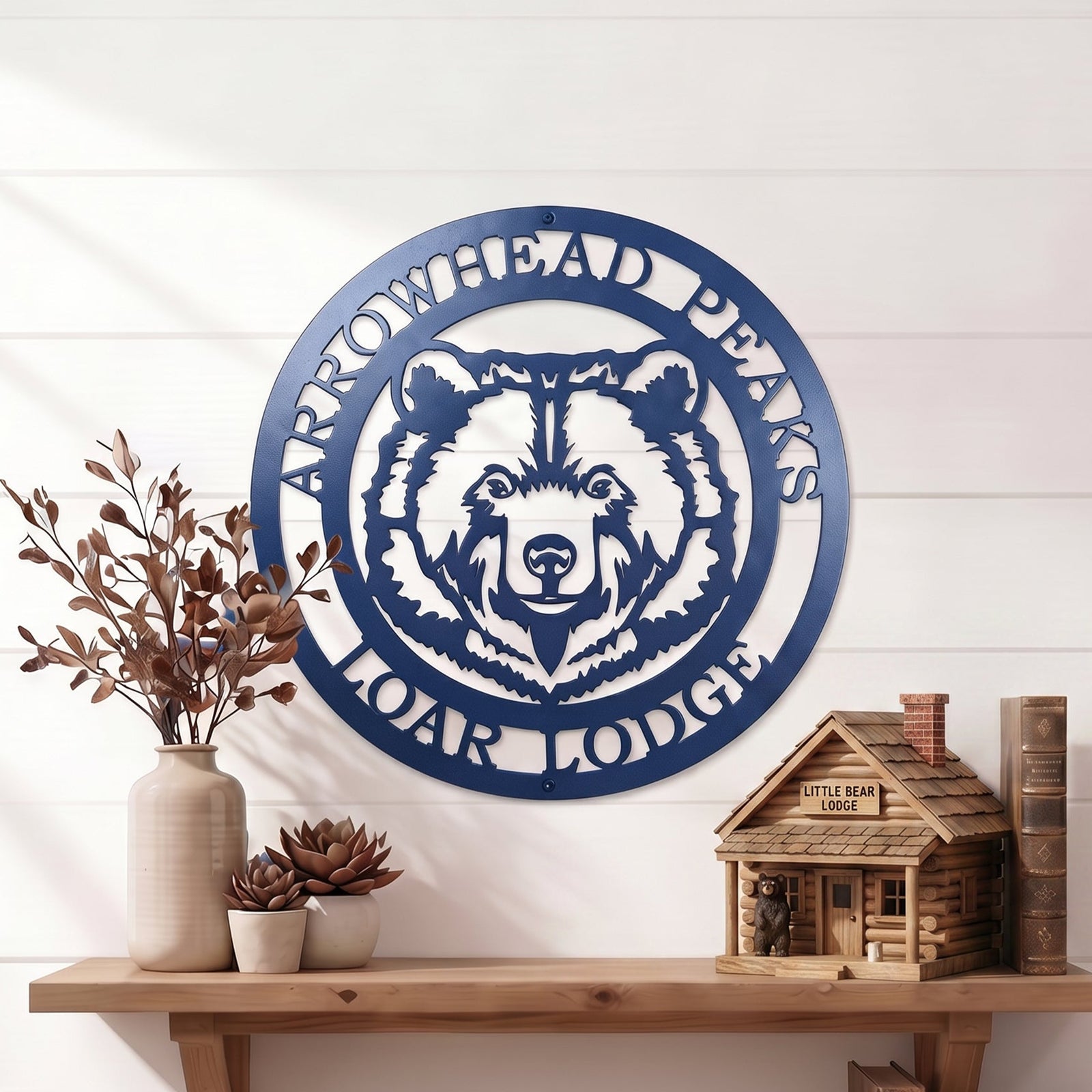 Custom Arrowhead Peaks Bear Lodge metal sign mounted above wooden shelf with books and decorative plants on white shiplap wall