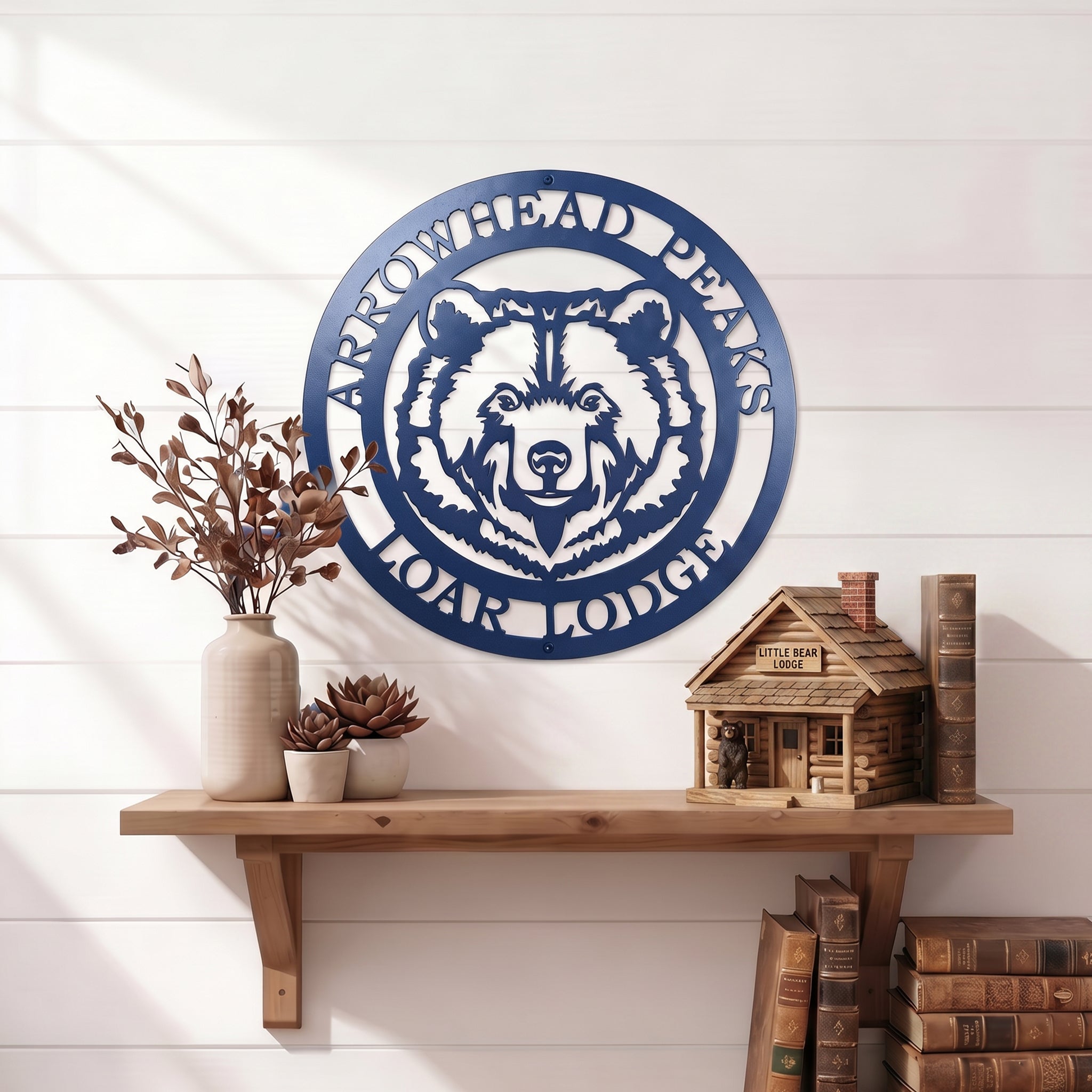 Custom Arrowhead Peaks Bear Lodge metal sign mounted above wooden shelf with books and decorative plants on white shiplap wall