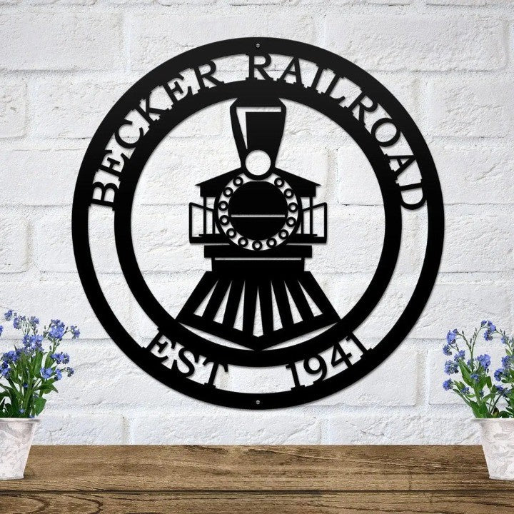 Black metal locomotive wall plaque with personalized name and year mounted on white brick with floral accents.