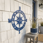 Blue personalized compass rose metal sign with custom coordinates and beach name mounted on a coastal porch wall