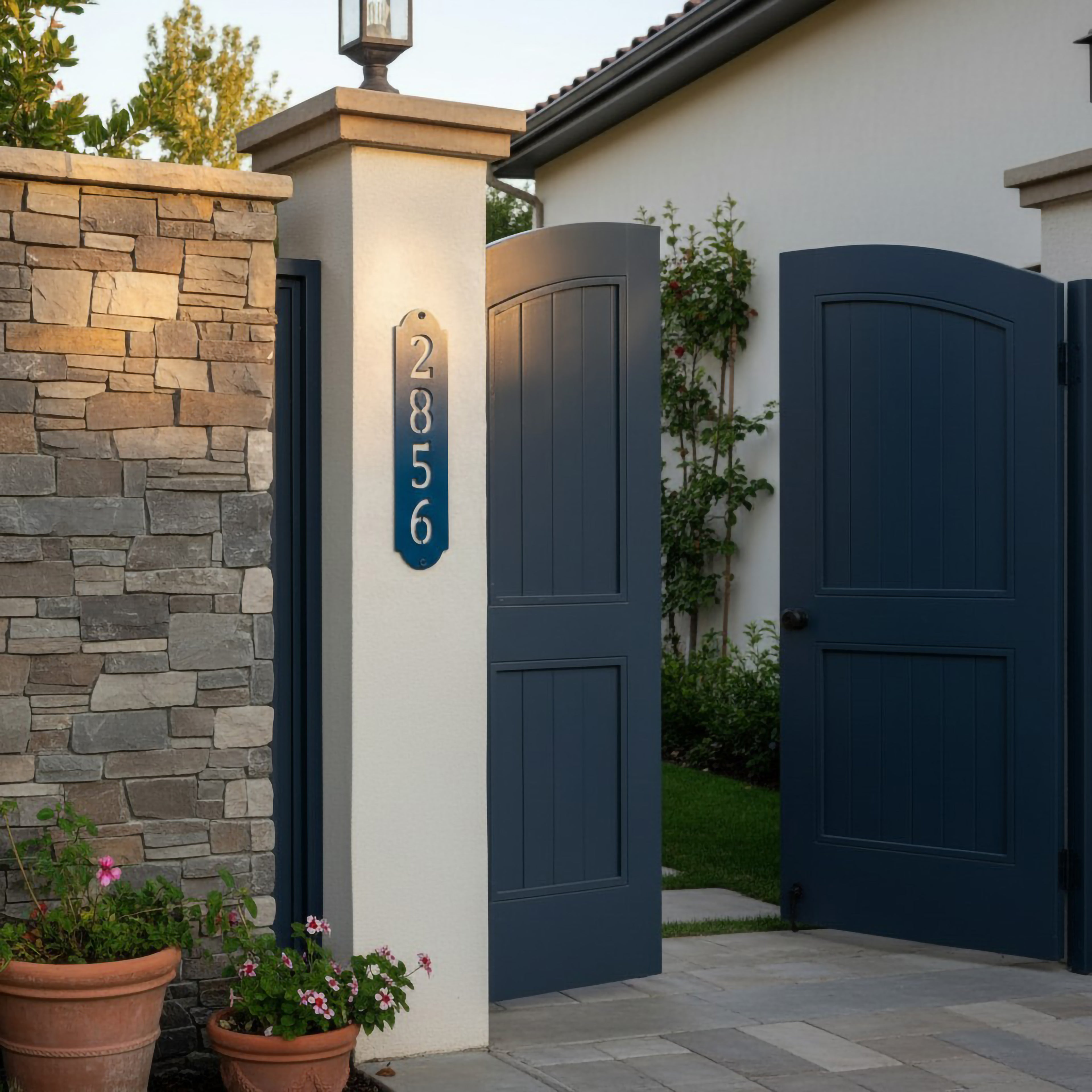 Bright blue vertical house number plaque mounted on a stucco gate pillar beside a blue entry gate