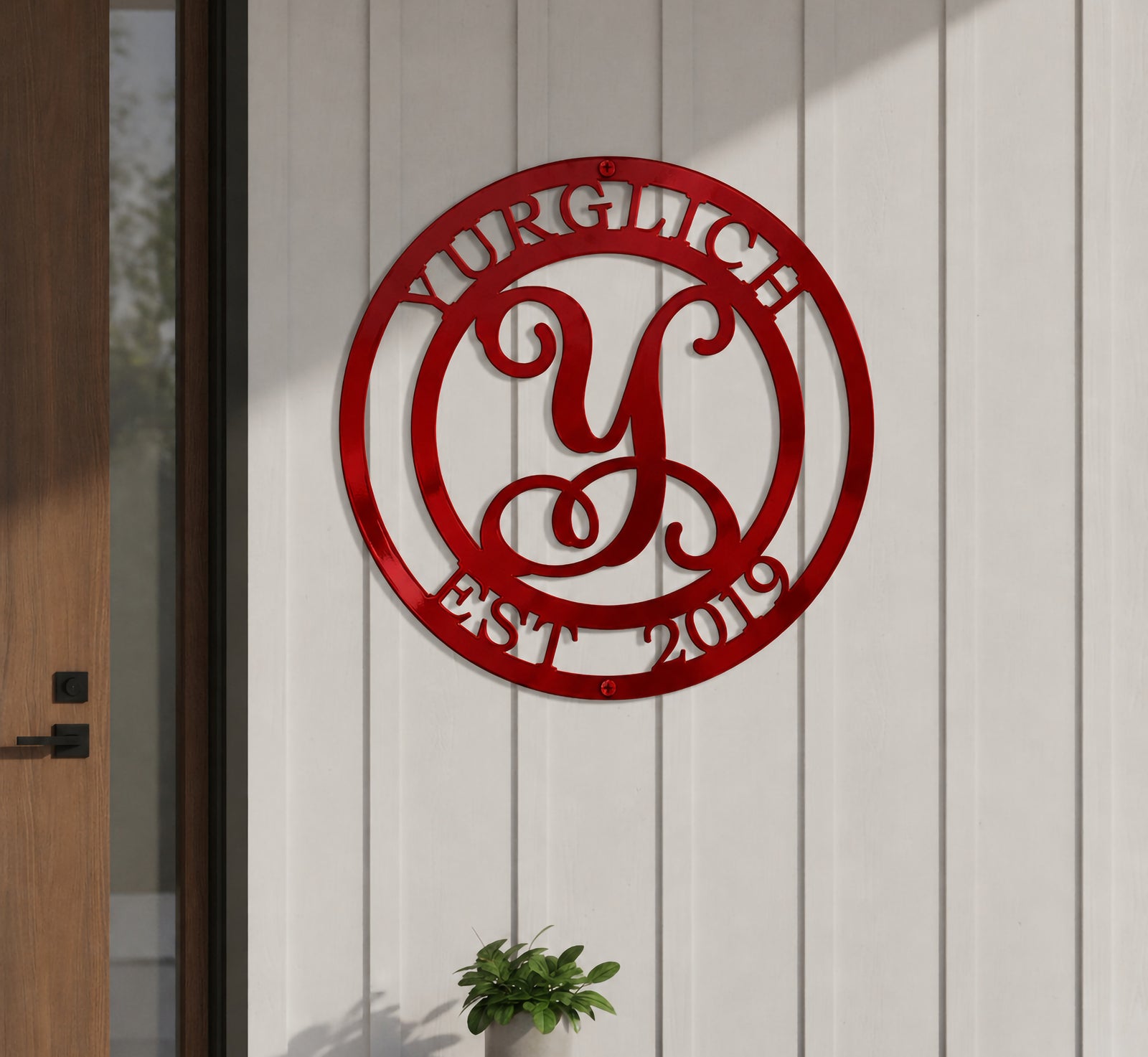 Shiny candy apple red finish of the personalized metal script letter monogram sign mounted on white vertical wood siding next to an entryway.