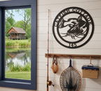 Matte black personalized catfish cabin metal sign with custom text Catfish Cottage 145 mounted on white shiplap next to a window overlooking a lake and cabin.