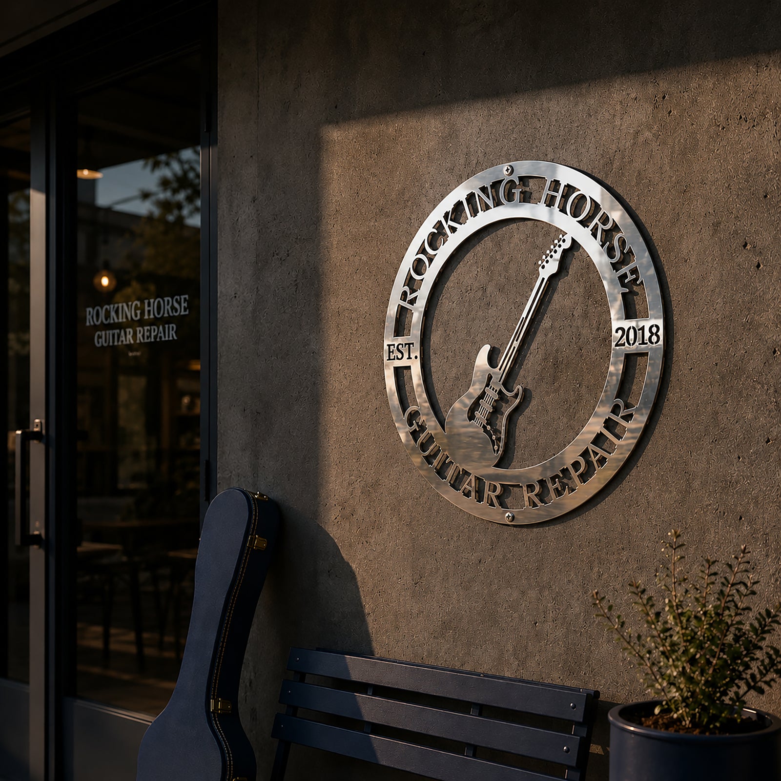 Polished chrome silver personalized electric guitar metal sign catching sunlight on a concrete wall outside a music studio entrance.