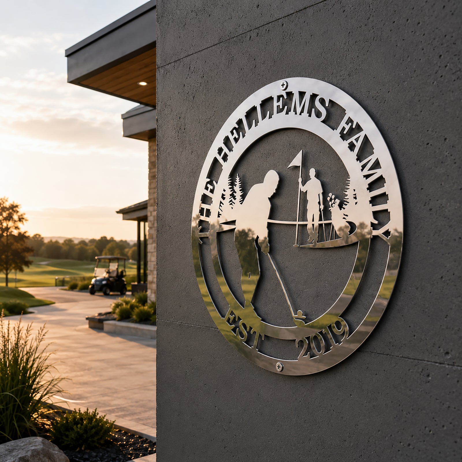 Polished chrome silver personalized golf theme metal sign mounted outdoors on a textured grey concrete pillar looking out to a golf course walkway with a parked golf cart at sunset.