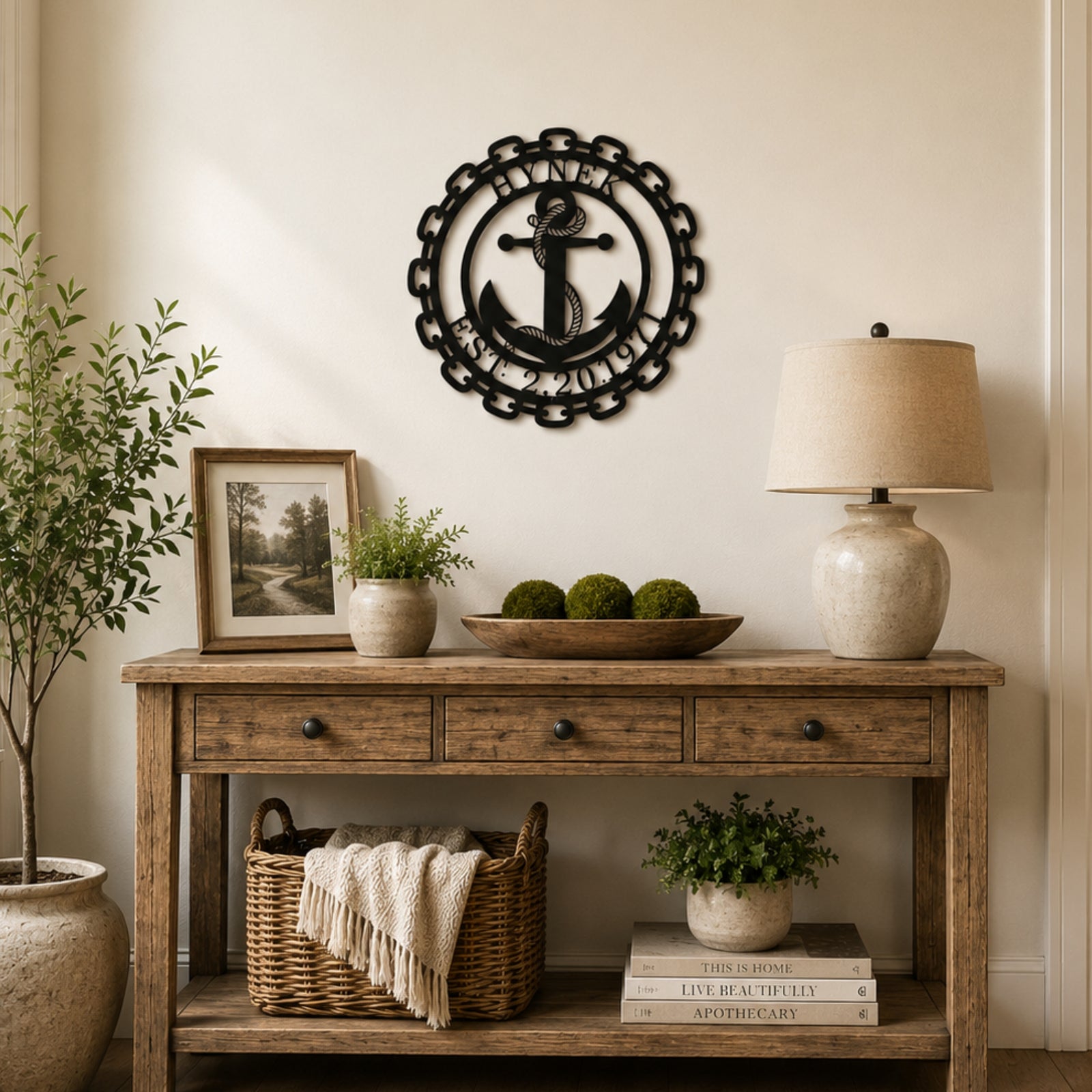 Custom nautical anchor metal wall decor with family name and established date styled above wooden entryway table with lamp and greenery