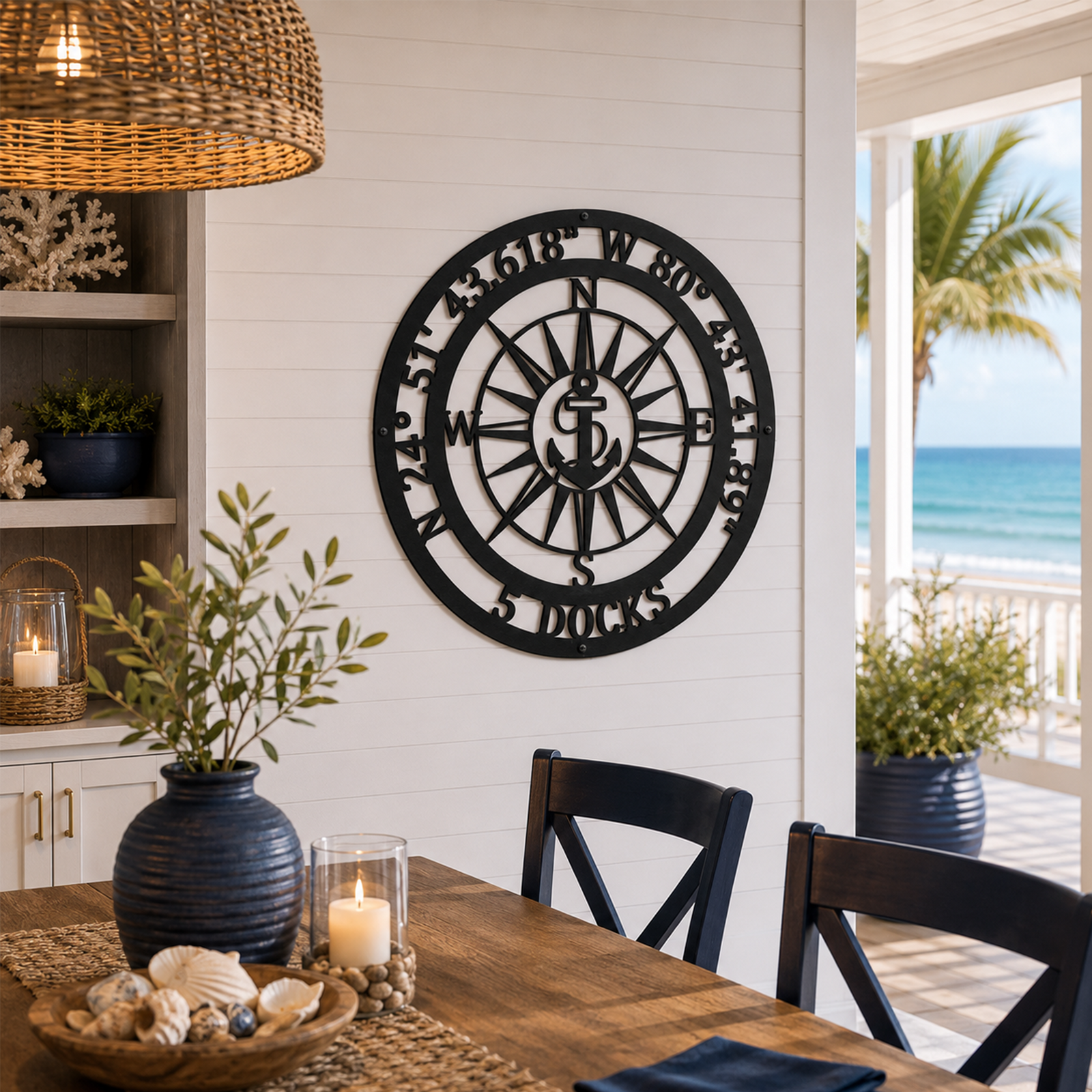 Custom laser-cut black metal coordinates sign with an anchor compass design displayed on a white shiplap wall in a nautical-style beach house dining area.