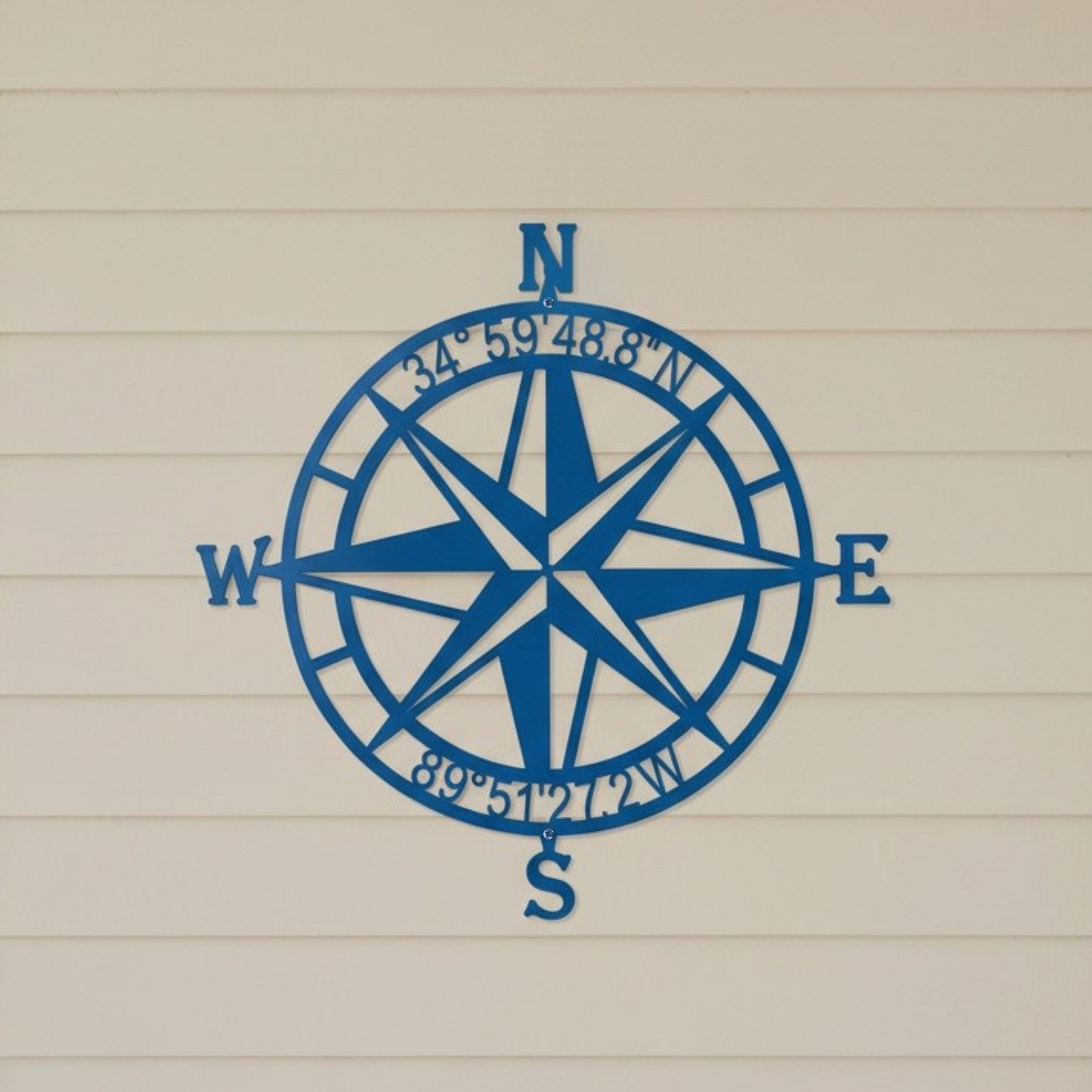 Custom compass rose metal sign — personalized latitude longitude wall decor in blue powder-coated steel mounted on a coastal-inspired exterior wall.